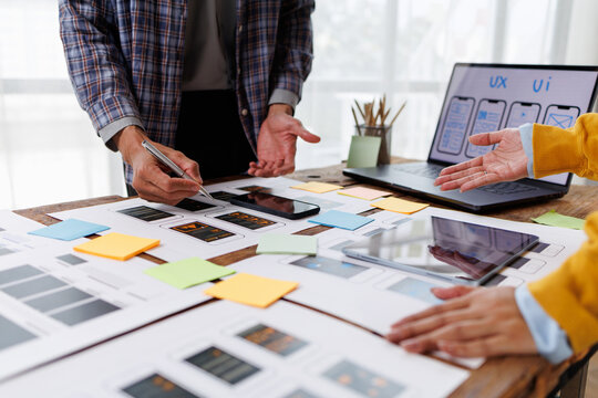Experienced designers brainstorming and working on a mobile app user interface. Reviewing screen layouts and interactive elements on paper printouts