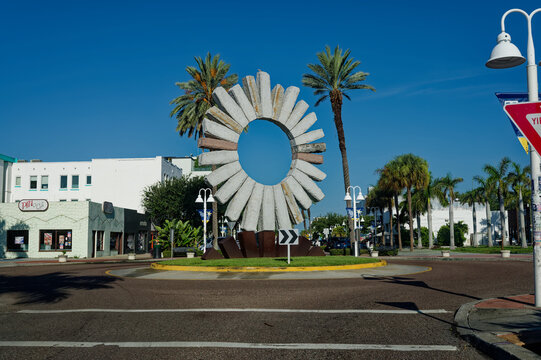 A circular concrete Sculpture The Sun on the EDGE Editorial Use Only July 23, 2026 St. Petersburg,FL USA dominates a downtown roundabout framed by tall palm trees and a bright blue sky, creating a tro