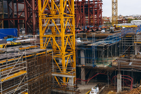 Yellow crane rises above red steel framing and rows of scaffolding across a wide building site. Large scale urban development and construction investment shaping skylines and property markets
