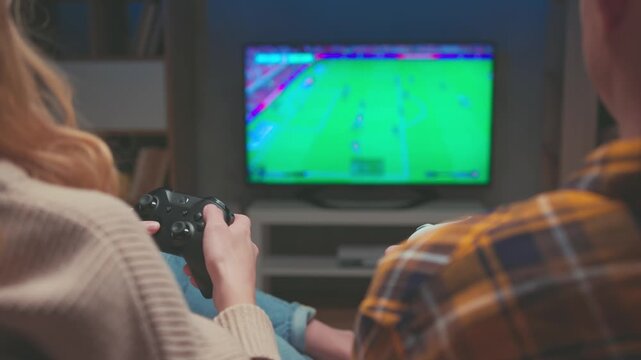 Woman Holding Black Gamepad Controller while Playing Football Console Game. Unrecognizable Female Competes in Soccer Match Next to Male Partner. Family Leisure and Modern Entertainment Tech 4k