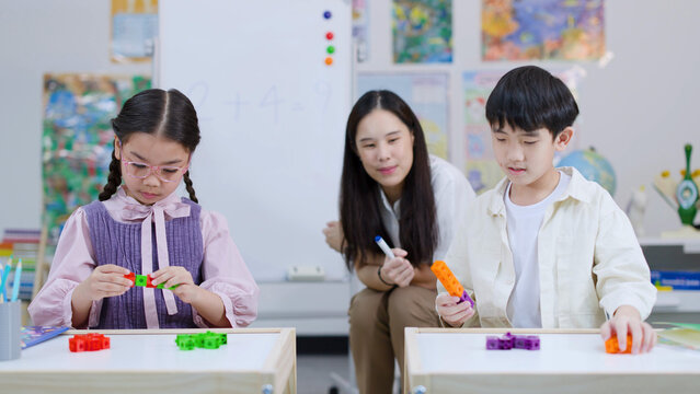 Asian Teacher Supervising Two Students Using Colorful Math Counting Blocks