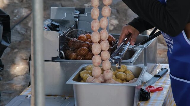 Street vendor deep frying traditional Thai Luk Chin Moo Ping pork balls in hot bubbling oil at an outdoor Thai street market. Street food concept