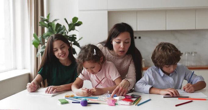 Adult mother spending quality time with three children in domestic kitchen, siblings sitting at table, drawing pictures with colored pencils. Family interaction, creative activity, kids development