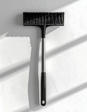 Black brush with handle against white wall.