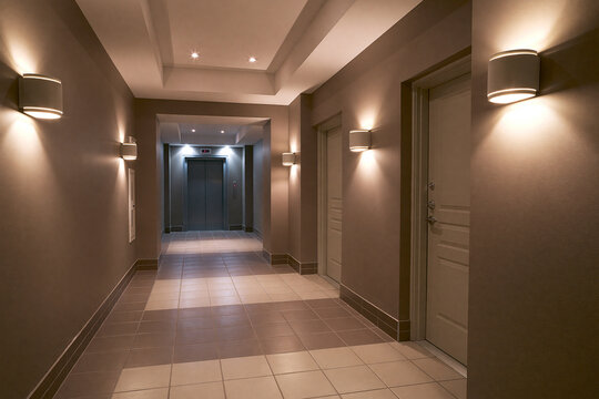 Modern illuminated hallway with elevator and doors in a residential building.