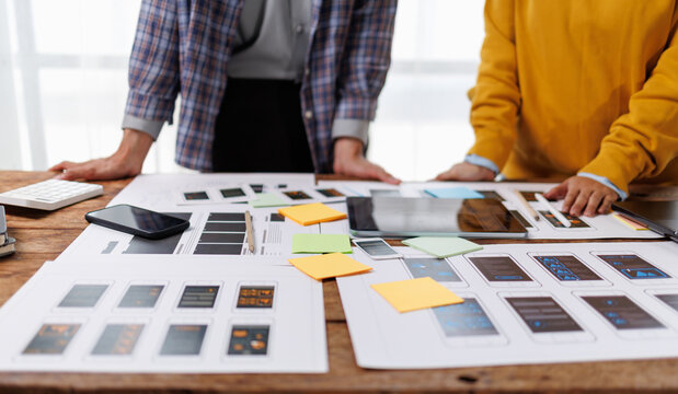 Experienced uxui designers actively developing a mobile app interface, reviewing wireframes and prototypes for optimal user experience and digital product creation on a wooden desk