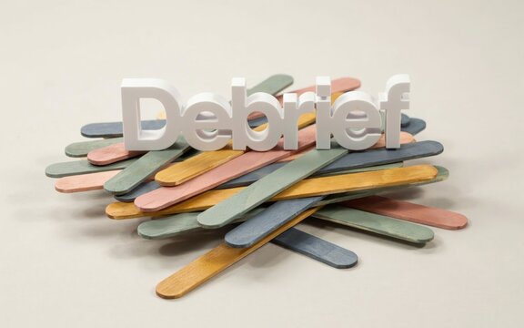 Debrief 3D white text on colorful wooden sticks. Business meeting debriefing concept with pastel craft sticks. Corporate review and feedback session visual.