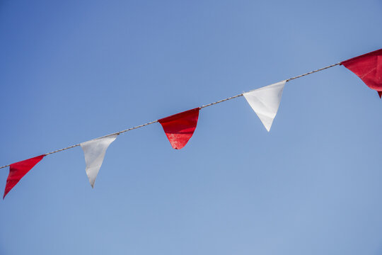 Red And White Pennant Bunting Flags Against Clear Blue Sky For Outdoor Party And Celebration
