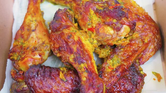 Spicy seasoned roasted chicken pieces in takeout box close up