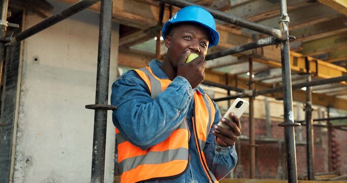Apple, break and man at construction site with phone, fruit snack and PPE for building project. Black person, reflection and eating lunch outdoor with helmet, tech and rest with infrastructure plan