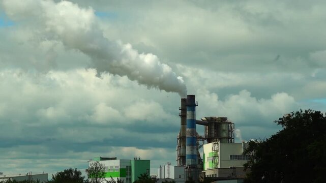 A video taken in Mosty, Belarus, on July 19, 2026, shows a factory with smoke billowing from its chimney. The sky is cloudy, making it clear it's midday. The area appears industrial and bustling.