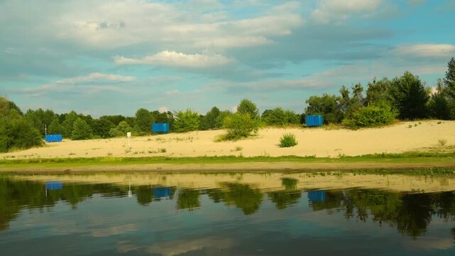A view from the gunboat, with trees and clouds clearly reflected on the sandy shore. Along the riverbank in a natural setting in daylight, in the city of Pinsk, Belarus, on the Pina River embankment, 