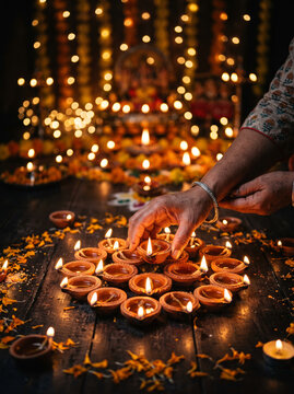 Hands lighting multiple clay diya oil lamps arranged in circle for Diwali celebration night