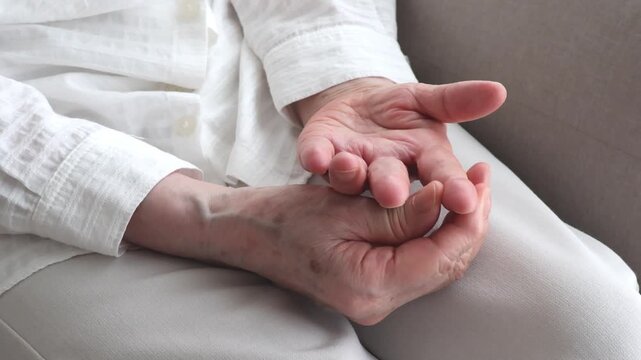 An elderly woman massaging her hands on her lap.