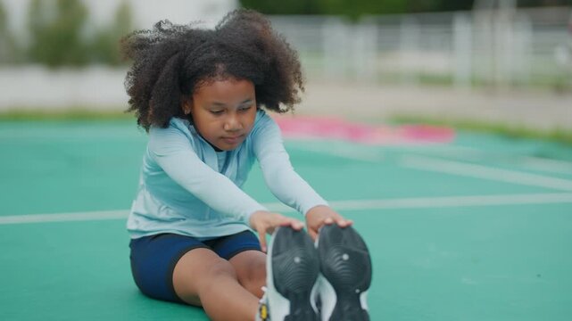 Young girl stretches on green court. She smiles with joyful energy. Her hair bounces with movement. Athletic wear suits her activity. Great for fitness or youth sports