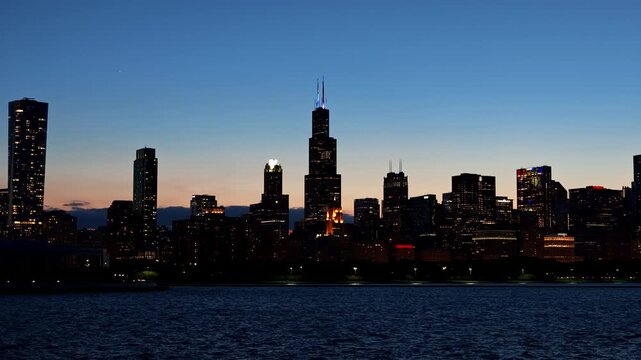 Chicago skyline at blue hour across Lake Michigan, featuring illuminated downtown skyscrapers reflected against a deep blue evening sky.