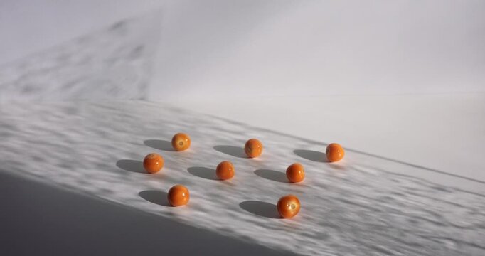 Small orange fruits sit on a white rippled surface that casts long shadows across the scene to provide a high quality background with ample empty space for overlaying text or other design elements.