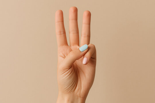 Hand showing three fingers with pastel blue nail polish against beige background, gesture concept for counting or number three sign