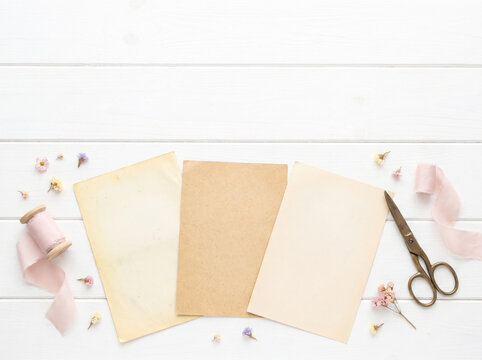 Blank paper sheets with scissors and pink ribbon on a rustic white wood table