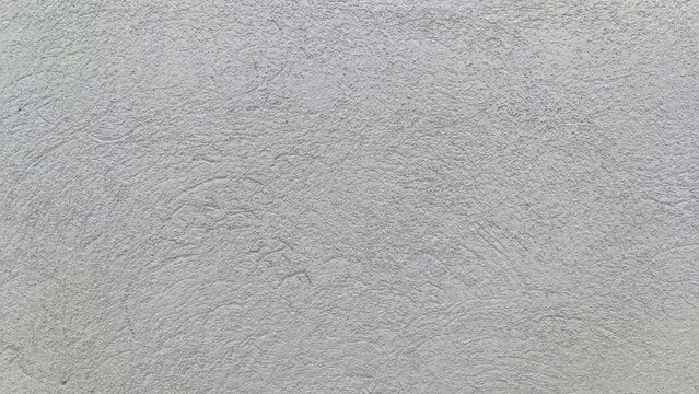 Close up of a hand troweled light gray concrete wall with granular bumps and swirling patterns, creating a neutral, utilitarian surface texture.
