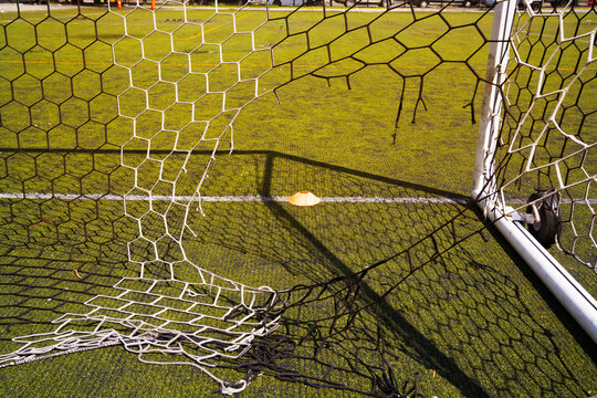 A documentary style shot of a soccer ball resting inside a net after a goal, set against artificial turf, capturing an energetic sports atmosphere.
