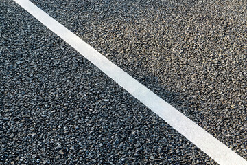 Fototapeta premium A close-up view of asphalt pavement featuring a diagonal white traffic marking line, showing surface texture and aggregate details.