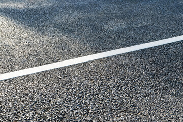 Fototapeta premium A close-up view of textured asphalt pavement with a straight white road marking line, part of urban transport infrastructure.