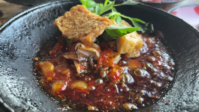 Close up view of hot sambal Gami on the earthenware plate. spicy, chilly, tomatoes. tempe, tahu. squid. Indonesian traditional food. Bontang, East Kalimantan. paste. black. close up view.