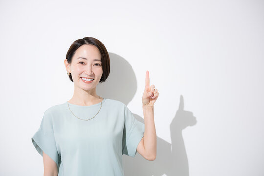 A half-body shot of a Japanese woman in a short-sleeved shirt, smiling and pointing to provide directions, looking directly at the camera&mdash;an illustrative image for announcements, key points, and other