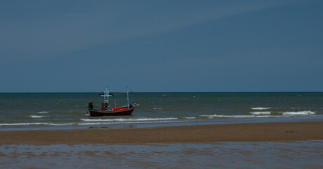 Obraz premium Traditional Fishing Boat Anchored Near a Beach Under Dark Storm Clouds