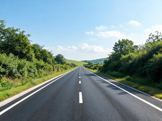 Obraz premium A straight paved road stretches through lush green rural landscape under a clear blue sky with distant rolling hills.