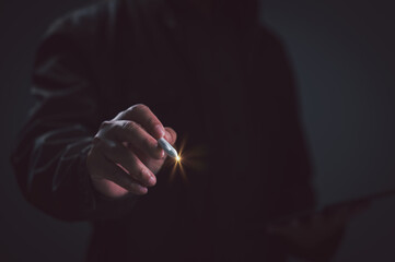 Unrecognizable businessman wearing black jacket holds glowing stylus pen pointing forward inside dark studio setting representing digital technology innovation interactive design concept. © Mdisk