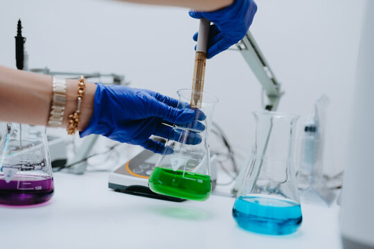 Scientist Wearing Gloves Conducting Chemical Experiment With Colorful Liquids In Laboratory Beakers