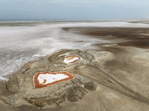 Saline ponds with ruddy algae growth and white salt deposits at the Atlantic Coast. Aerial view. Drone shot. Namib Desert, Skeleton Coast, Dorob National Park, Namibia