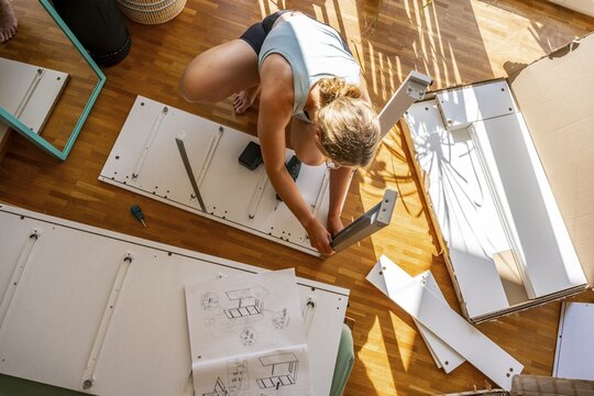 Young woman setting up a shelf, furniture assembly with screwdriver, IKEA furniture in a new apartment, moving