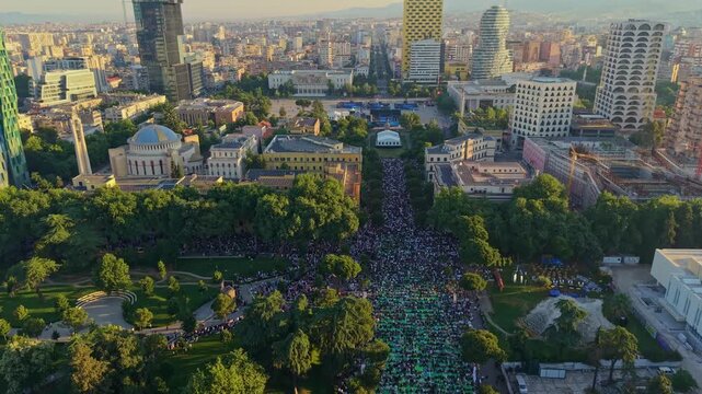 Aerial view of a massive crowd gathering for Eid Mubarak morning prayers in a beautiful park in Tirana, Albania, during the sunrise golden hour.