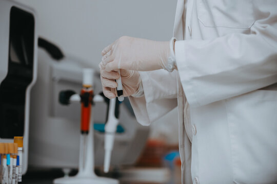 Scientist In White Lab Coat Holding Test Tube Sample With Pipettes And Medical Equipment In Laboratory