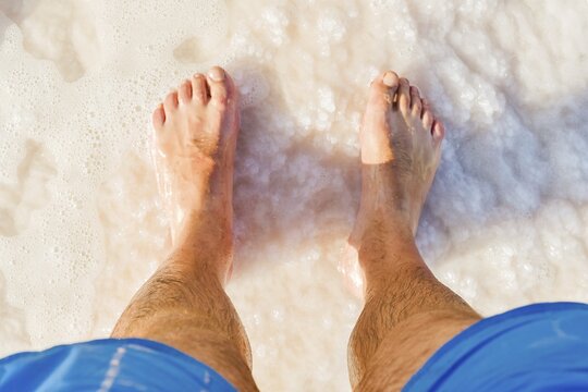 Close-up POV male tourist walking on the unique salt formations and turquoise mineral-rich waters of the Dead Sea beach. A concept for wellness, healthy living, and natural spa travel
