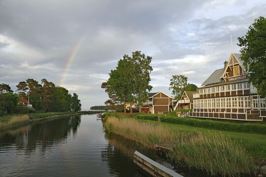 Beautiful rainbow over a quiet river landscape with traditional wooden buildings and green trees, old hotel, Karlsborg, V&auml;stra G&ouml;talands l&auml;n, Sweden