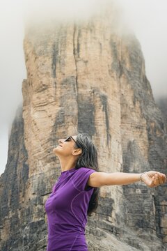 Woman outstretching arms breathing deep misty towering rock wall backdrop Tre Cime di Lavaredo Dolomites Alps Italy summer landscape