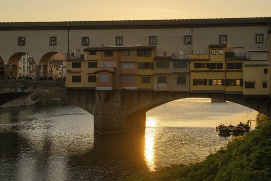 Sun rays reflect on the Arno River, crowd on the historic Ponte Vecchio, evening mood, old town, Florence, Tuscany, Italy