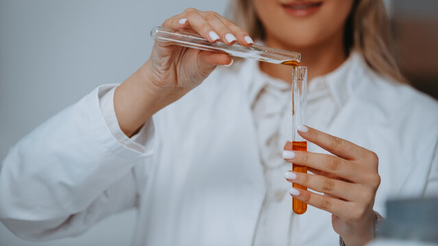Female Scientist Pouring Amber Liquid Between Test Tubes in Laboratory Cosmetic Chemistry Experiment