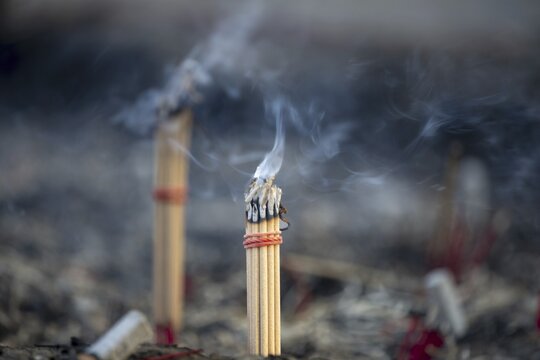 Fine smoke rises between the upright incense sticks and forms soft, swirling lines in the warm air. The bundles are carefully tied and depict a serene scene of traditional offerings such as those found in many temples and shrines, Wat Yai Chai Mongkon, Ayutthaya, Thailand