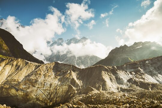 Georgia Svaneti Shkhara glacier summer morning with clouds drift across rugged peaks, moraine rocks foreground .Smoky mountains concept