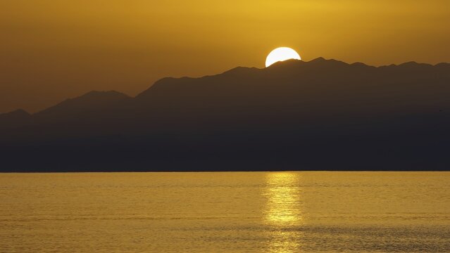 The sun sets behind the mountains and illuminates the sea golden, Matala, South Coast, Crete, Greek Islands, Greece