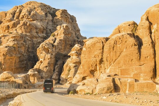 Black passenger coach bus driving asphalt road winding through sandstone rock mountains canyon desert landscape leading ancient archaeological tourist attraction Little Petra Jordan