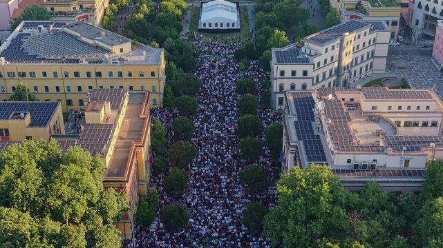 Aerial view of a massive crowd gathering for Eid Mubarak morning prayers in a beautiful park in Tirana, Albania, during the sunrise golden hour.