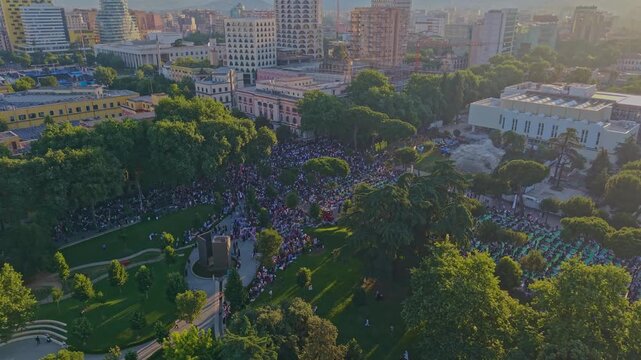 Aerial view of a massive crowd gathering for Eid Mubarak morning prayers in a beautiful park in Tirana, Albania, during the sunrise golden hour.