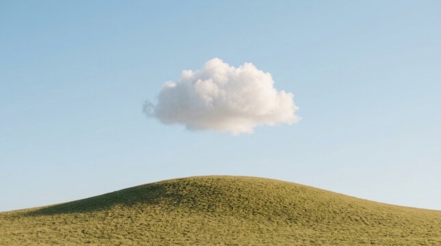 Lone fluffy cloud above rolling green hill under clear blue sky.