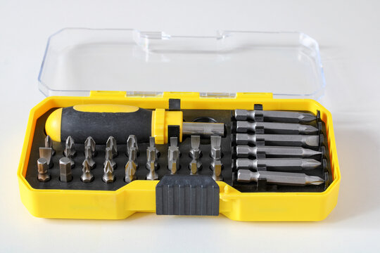 A open yellow plastic case containing a screwdriver handle and replaceable drill bits resting on a white background.